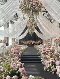 an aisle with flowers and white draping on the ceiling is decorated for a wedding