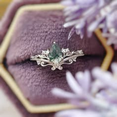 an engagement ring with a green stone surrounded by white diamonds on top of purple velvet