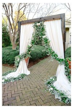 a wedding arch decorated with greenery and white draping for an outdoor ceremony