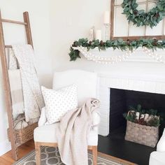 a living room decorated for christmas with white furniture and greenery on the mantel