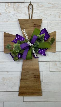 a wooden cross decorated with purple and green ribbons on a white wood wall behind it