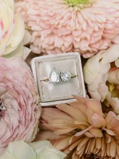 two engagement rings sitting on top of a box surrounded by pink flowers and peonies