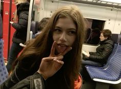 a woman making a funny face while sitting on a train with her finger in her mouth