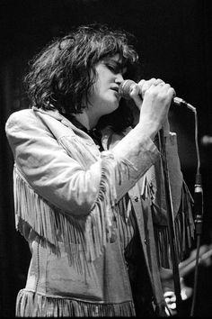 black and white photograph of a woman singing into a microphone with fringes on it