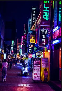 a city street at night with neon signs on the buildings and people walking down the sidewalk