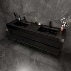 a bathroom with two black sinks and grey tile flooring on the walls, in front of a gray tiled wall