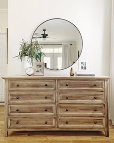 a dresser with a round mirror on top and a plant in the middle next to it