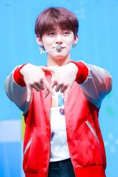 the boy is making a heart sign with his hands while standing in front of a blue background