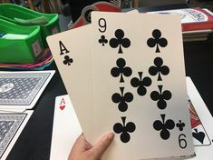 two hands holding four playing cards in front of each other on a table with green bins