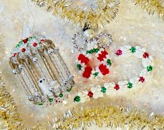 two christmas ornaments are laying next to each other on a table covered in tinsel