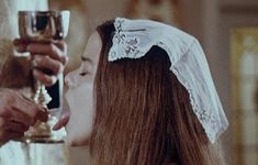 a woman in a wedding dress holding a wine glass and kissing the man's forehead