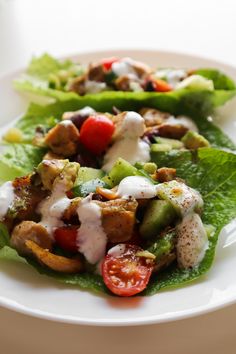 two lettuce wraps with chicken, tomatoes and dressing on them sitting on a white plate