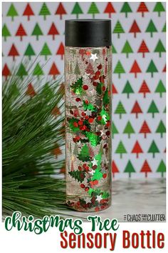 a christmas tree in a glass bottle filled with confetti next to pine branches