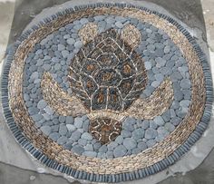 a circular mosaic on the ground with rocks and stones around it, depicting an animal's head