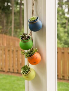 three hanging pots filled with succulents on a white porch wall next to a wooden fence