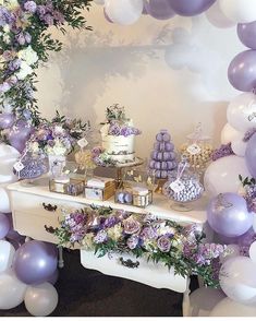 a table topped with lots of purple and white balloons next to a cake on top of a table