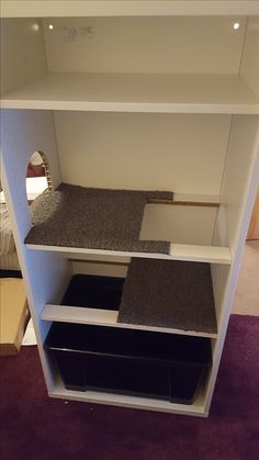 a white book shelf with black bins and carpet on the bottom floor in front of a bed