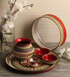 a red and gold plate with two cups on it next to a vase filled with white flowers