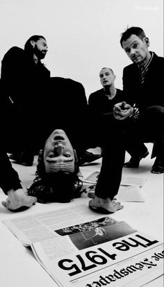 three men sitting on the ground with their heads down in front of them, and one man holding a cell phone up to his ear