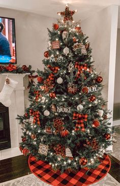 a christmas tree decorated with red, white and black plaid ornaments in front of a fireplace