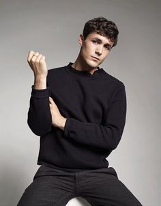 a young man sitting on top of a white stool wearing a black sweater and pants