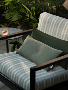 a chair with pillows on it sitting in front of a table and potted plants