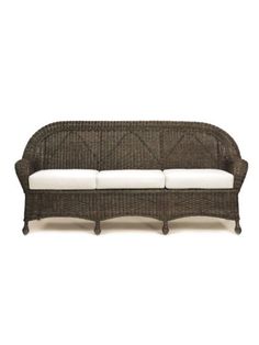 a wicker couch with white cushions on it's back legs and arms, against a