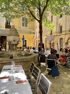 people are sitting at tables in an outdoor restaurant with water fountain on the side walk