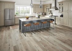 a kitchen with wooden floors and stainless steel appliances, including an island counter that has four stools in front of it