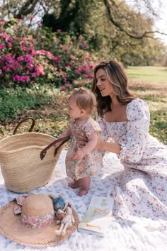 a woman holding a baby on top of a blanket next to a basket and book