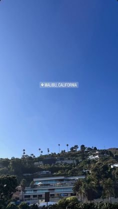 an airplane flying over the top of a building on a hill with palm trees in front of it