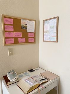 a desk with a book, cell phone and sticky notes on the wall above it