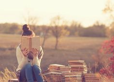 a woman sitting on the ground reading a book with stacks of books in front of her