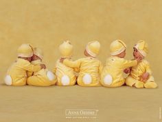 four babies in yellow onesuits sitting on the ground with their backs to each other