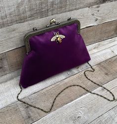 Stunning, handmade, purple velvet clutch bag with bee detail. The pattern of the lining inside of the bag may vary. But don't worry, I always make sure the lining of the bag matches the outside beautifully. Use it as a classic clutch or attach the shoulder strap to wear over your shoulder or as a crossbody. - Bronze colour Chain strap (detachable) - Bronze colour Kiss lock clasp - H:19cm x W:29cm x D:4cm approximately - Metal clasp width: 20cm - Tiger eye stone detail (The markings on the stone Purple Pouch Clutch As Gift, Velvet Pouch Bag For Gifts, Velvet Pouch Bag For Gift, Velvet Pouch Bag As Gift, Handmade Velvet Rectangular Bags, Gold Velvet Bag For Gifts, Velvet Evening Bag As A Gift, Elegant Purple Clutch For Everyday Use, Handmade Rectangular Velvet Bag