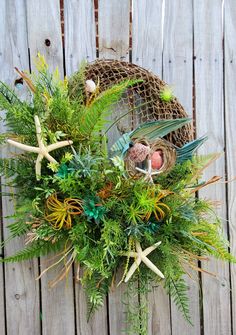 an arrangement of plants and seashells in a basket on top of a wooden fence