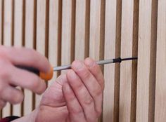 a person is using a screwdriver to fix a wooden wall with wood slats in the background