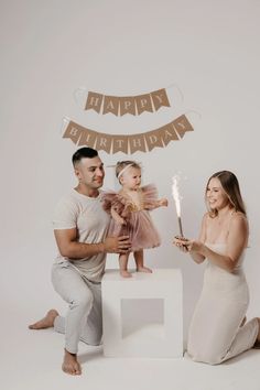 a man and woman holding a small child while sitting on a stool with a candle in their hand