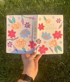 a person holding up an open bible in their hand with flowers on the front cover