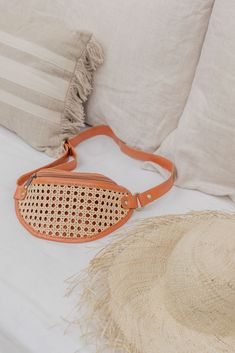 a straw hat sitting on top of a bed next to a tan purse and white pillows