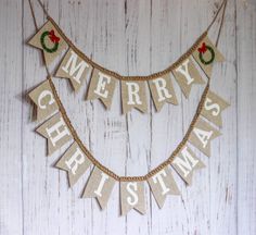 a merry christmas banner hanging on a white wooden wall with the words merry christmas spelled in red and green letters