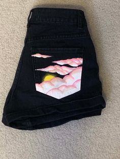 a pair of black jeans with pink and yellow clouds on the side, sitting on carpet