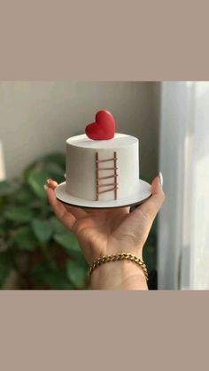 a hand holding a cake with a heart on top and a ladder design on the side