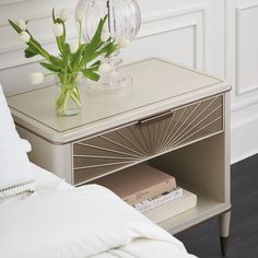 a vase with flowers sitting on top of a small table next to a white bed