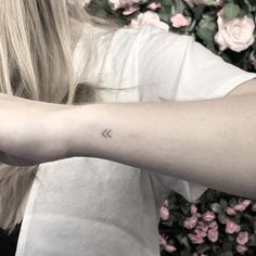 a woman's arm with a small arrow tattoo on the left side of her arm