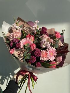 a bouquet of pink and white flowers is held by someone's hand in the sunlight