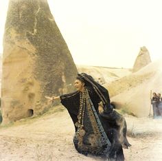 a woman dressed in black is walking through the sand with her hand out to someone