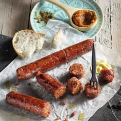 sausages and bread are on the table next to a bowl of dipping sauce, with a fork in it