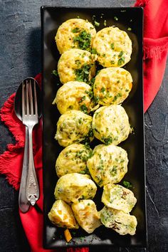 a black plate topped with biscuits covered in cheese and chives next to a fork