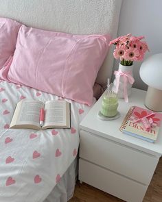 a bed with pink and white hearts on it, next to a book that is open